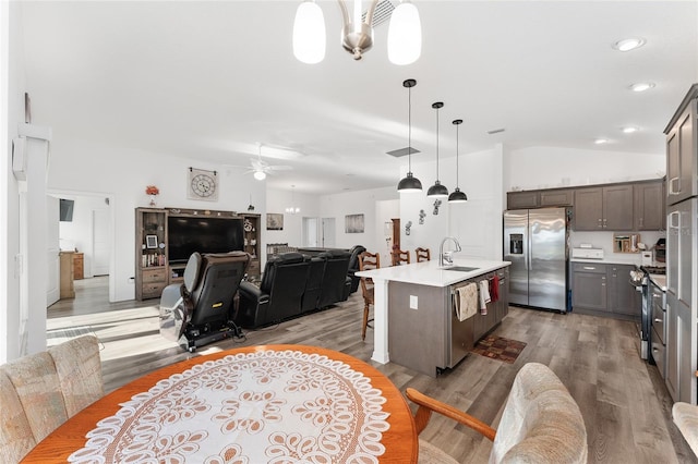 kitchen featuring appliances with stainless steel finishes, light wood-type flooring, ceiling fan, a center island with sink, and hanging light fixtures