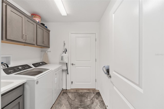 laundry room with washing machine and clothes dryer, cabinets, and a textured ceiling