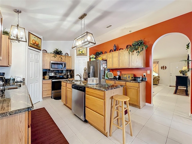 kitchen with a kitchen island with sink, light tile patterned floors, decorative light fixtures, and appliances with stainless steel finishes