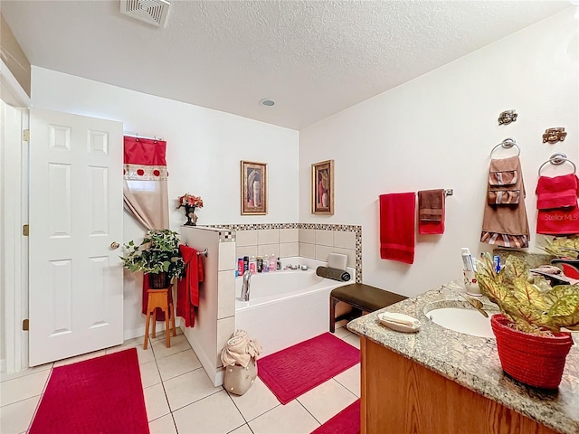 bathroom featuring a textured ceiling, vanity, a relaxing tiled tub, and tile patterned floors