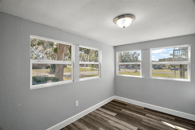 empty room with a textured ceiling, a healthy amount of sunlight, and dark wood-type flooring