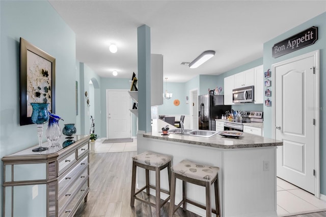 kitchen with a kitchen bar, stainless steel appliances, sink, white cabinets, and light hardwood / wood-style floors