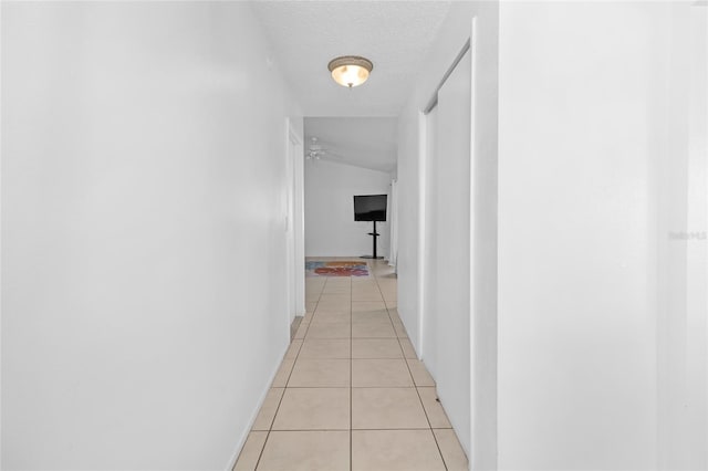 hall with light tile patterned floors, a textured ceiling, and vaulted ceiling