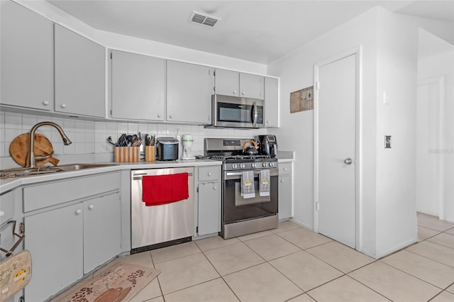 kitchen featuring gray cabinetry, sink, appliances with stainless steel finishes, tasteful backsplash, and light tile patterned flooring