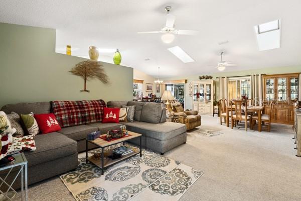 living room featuring ceiling fan, vaulted ceiling with skylight, light carpet, and french doors