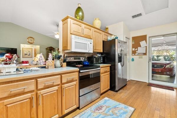 kitchen featuring ceiling fan, appliances with stainless steel finishes, decorative backsplash, light wood-type flooring, and vaulted ceiling