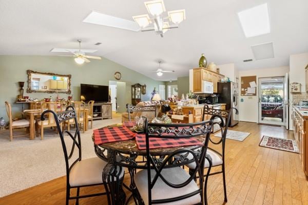 dining space with ceiling fan, vaulted ceiling with skylight, and light wood-type flooring