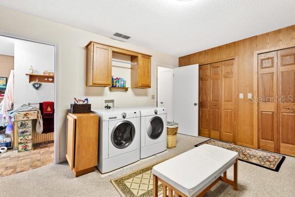 laundry area featuring cabinets, light colored carpet, washing machine and clothes dryer, and wooden walls