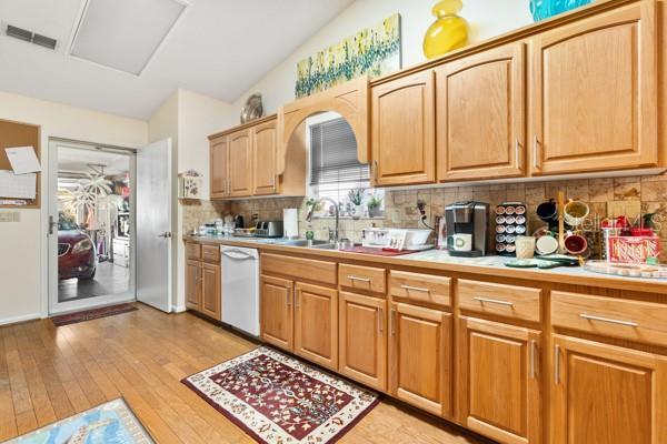 kitchen featuring light hardwood / wood-style floors, backsplash, white dishwasher, vaulted ceiling, and sink