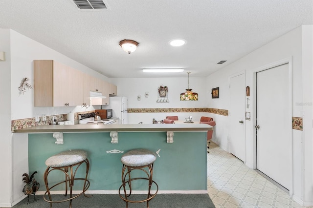 kitchen featuring a breakfast bar, light brown cabinets, kitchen peninsula, and range