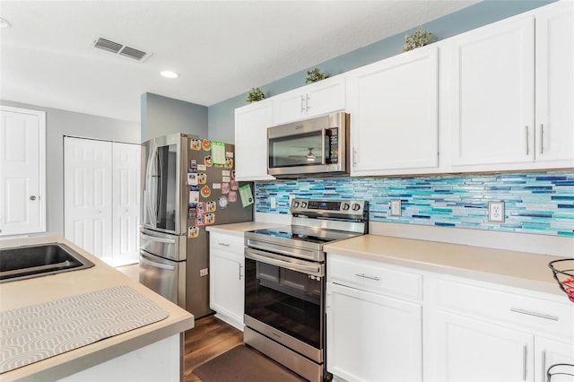 kitchen with appliances with stainless steel finishes, dark hardwood / wood-style flooring, backsplash, sink, and white cabinets