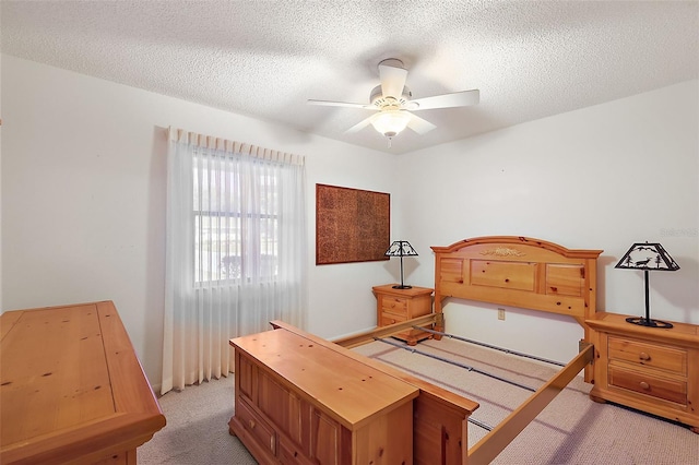 bedroom with ceiling fan, light colored carpet, and a textured ceiling