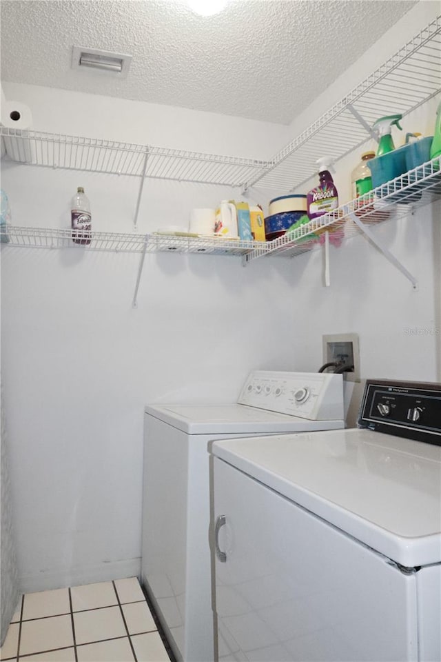 laundry area with separate washer and dryer, a textured ceiling, and light tile patterned floors