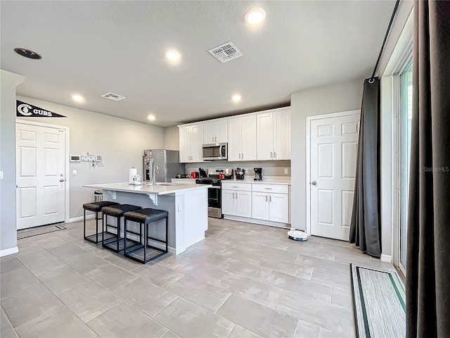 kitchen featuring sink, a breakfast bar area, a center island with sink, white cabinets, and appliances with stainless steel finishes