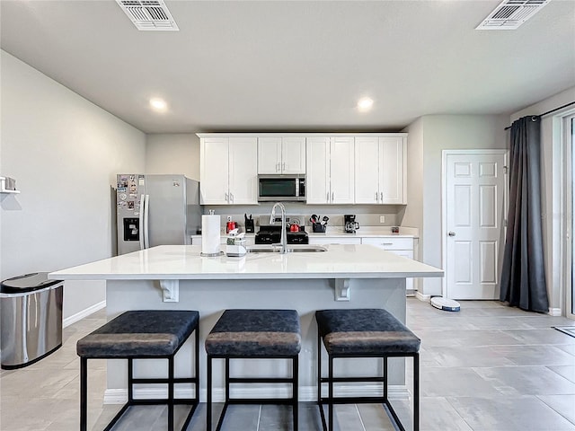 kitchen featuring a kitchen island with sink, white cabinets, sink, a kitchen bar, and stainless steel appliances