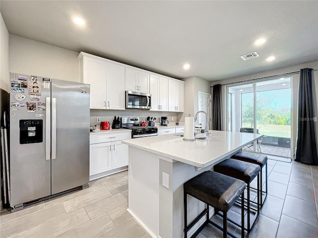 kitchen with a kitchen bar, white cabinets, an island with sink, and stainless steel appliances