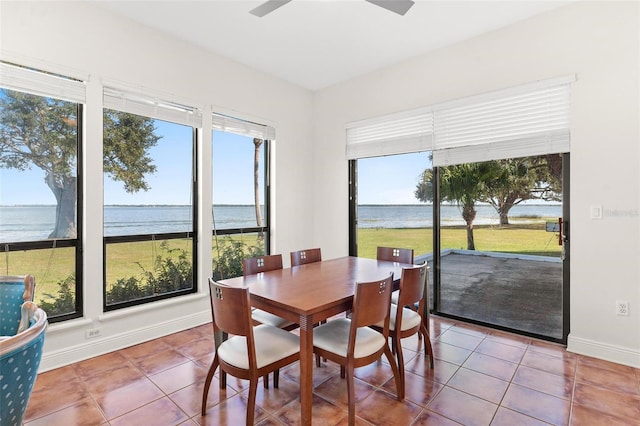 tiled dining room with ceiling fan and a water view