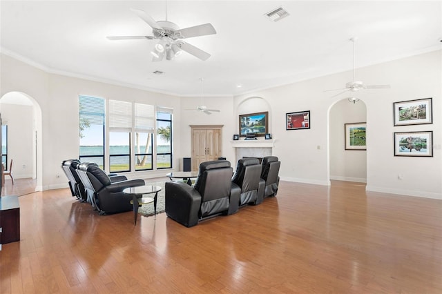 living room featuring ceiling fan, light hardwood / wood-style floors, a water view, and ornamental molding