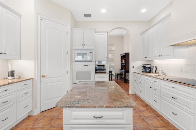 kitchen featuring white cabinetry, light stone counters, backsplash, white appliances, and a kitchen island