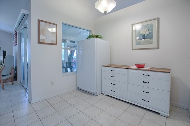 interior space featuring butcher block countertops, white cabinetry, light tile patterned floors, and white refrigerator