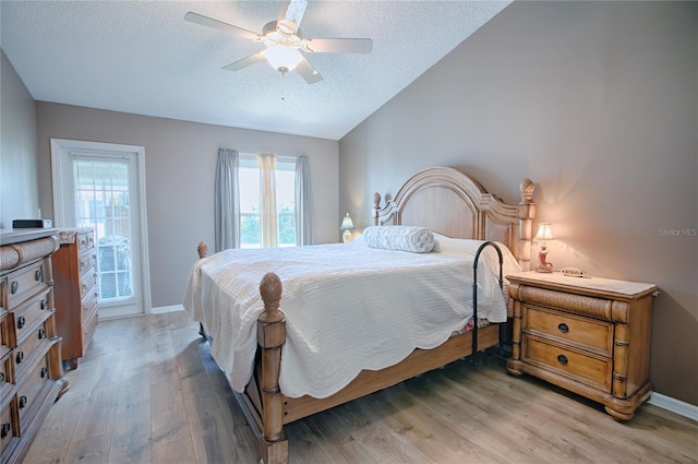 bedroom with a textured ceiling, ceiling fan, light hardwood / wood-style flooring, and vaulted ceiling