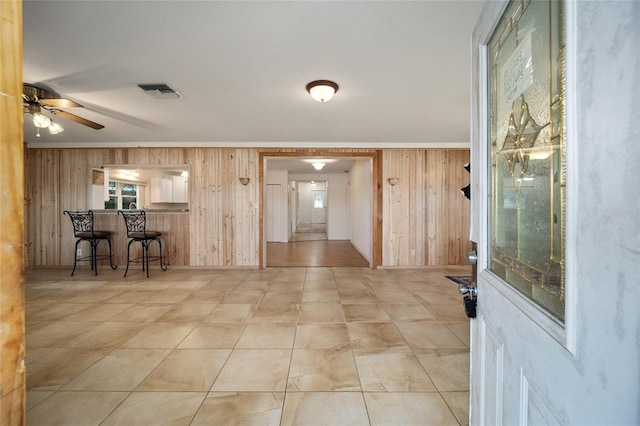 interior space with ceiling fan, ornamental molding, and wooden walls