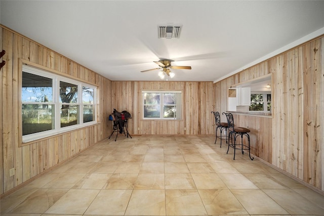 interior space featuring ceiling fan, wood walls, and indoor bar