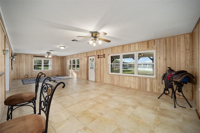 dining room featuring a textured ceiling, ceiling fan, and wooden walls