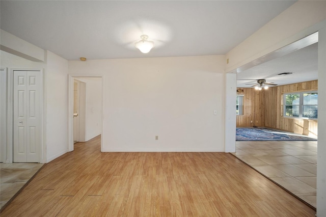 unfurnished room featuring light hardwood / wood-style flooring, ceiling fan, and wood walls