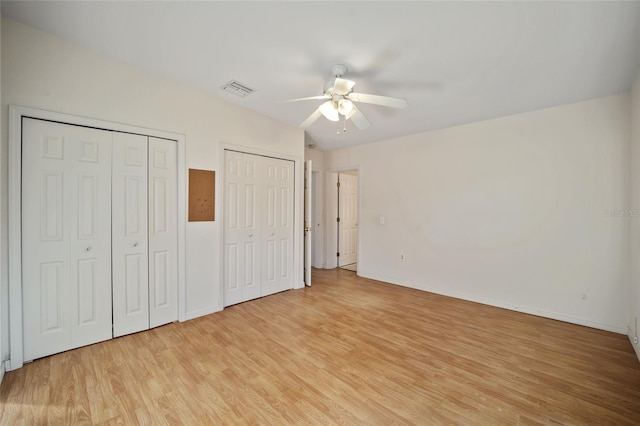 unfurnished bedroom with light wood-type flooring, ceiling fan, and multiple closets