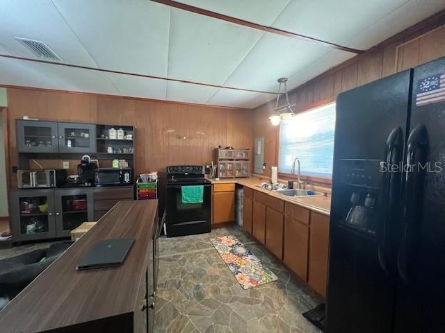 kitchen with hanging light fixtures, sink, wood walls, and black appliances