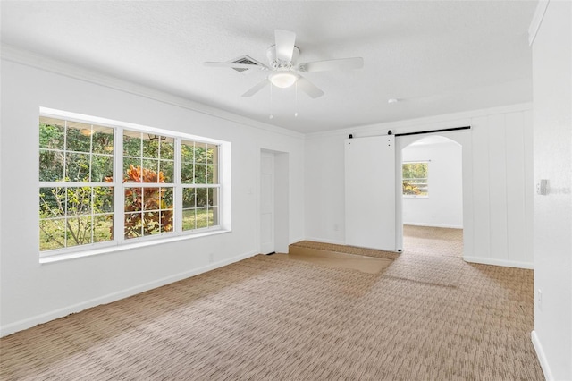 carpeted spare room with a textured ceiling, a barn door, ceiling fan, and ornamental molding