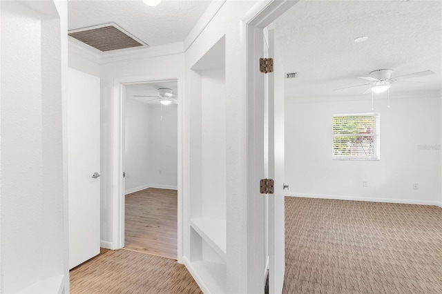 hallway with light hardwood / wood-style floors, a textured ceiling, and ornamental molding