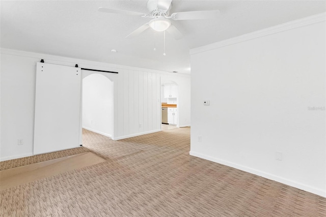 carpeted empty room featuring a barn door, crown molding, and ceiling fan