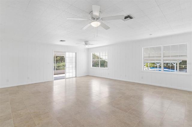 empty room featuring a wealth of natural light, wooden walls, and ceiling fan