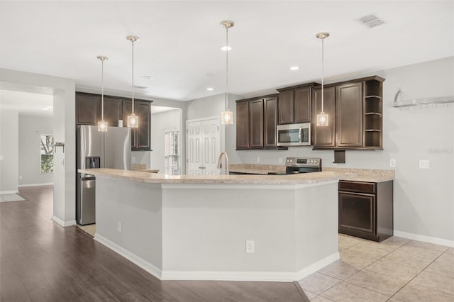 kitchen with appliances with stainless steel finishes, light wood-type flooring, dark brown cabinets, decorative light fixtures, and an island with sink