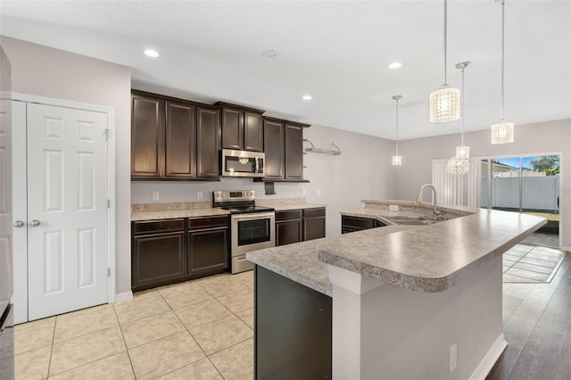 kitchen featuring appliances with stainless steel finishes, dark brown cabinets, sink, a center island with sink, and hanging light fixtures