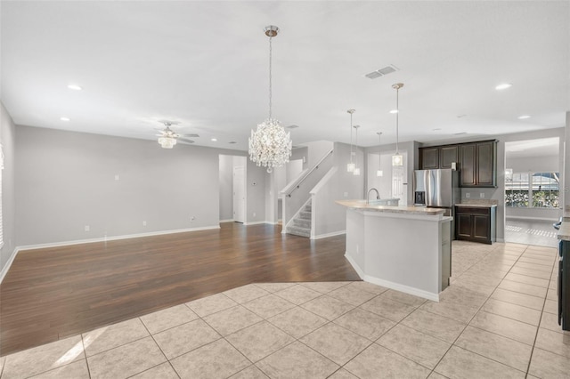 kitchen with a center island with sink, ceiling fan with notable chandelier, dark brown cabinets, light hardwood / wood-style floors, and stainless steel fridge with ice dispenser