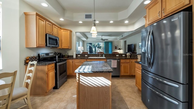 kitchen with stainless steel appliances, a raised ceiling, ceiling fan, dark stone countertops, and a kitchen island