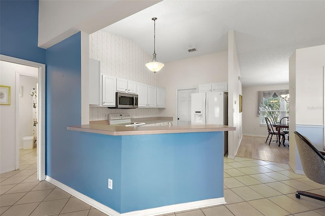 kitchen featuring pendant lighting, white appliances, white cabinets, vaulted ceiling, and kitchen peninsula