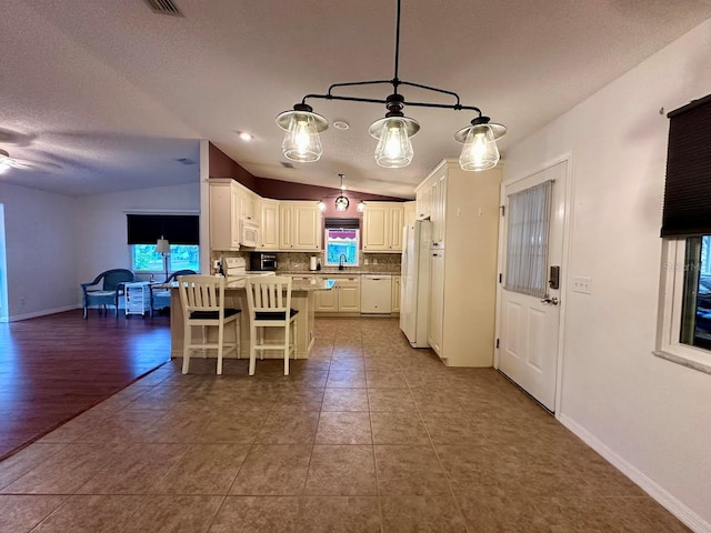 kitchen featuring backsplash, vaulted ceiling, decorative light fixtures, white cabinetry, and a breakfast bar area