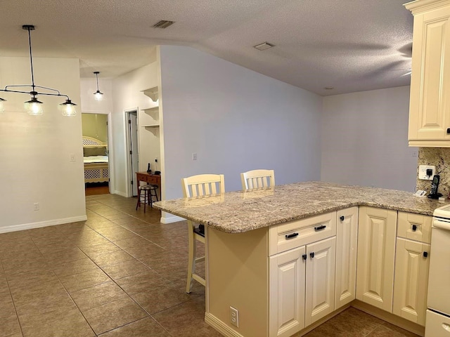 kitchen with kitchen peninsula, a kitchen breakfast bar, light stone countertops, dark tile patterned flooring, and hanging light fixtures