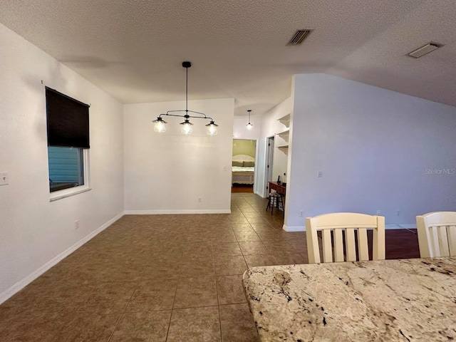 unfurnished dining area featuring dark tile patterned floors, a textured ceiling, and vaulted ceiling