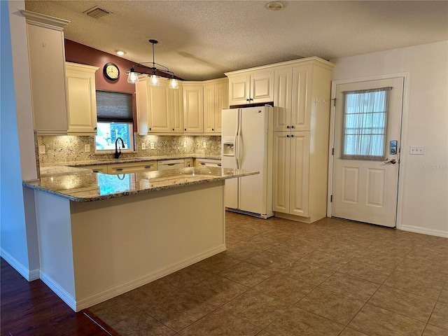 kitchen featuring hanging light fixtures, light stone countertops, white fridge with ice dispenser, and backsplash