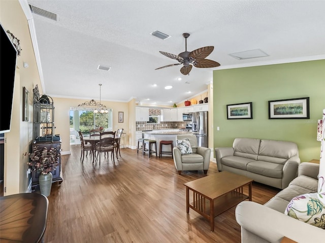 living room featuring a textured ceiling, vaulted ceiling, light hardwood / wood-style flooring, and ornamental molding