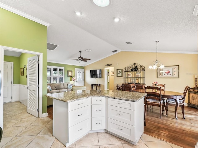 kitchen with light stone counters, ceiling fan with notable chandelier, pendant lighting, white cabinets, and a kitchen island