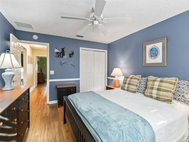 bedroom with ceiling fan, a closet, light hardwood / wood-style floors, and a textured ceiling