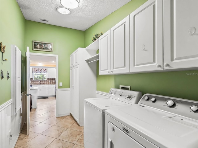 clothes washing area with washer and clothes dryer, cabinets, light tile patterned floors, and a textured ceiling