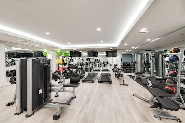 workout area featuring a tray ceiling and light wood-type flooring