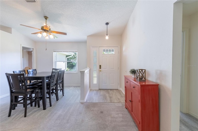 dining room with ceiling fan, light carpet, and a textured ceiling